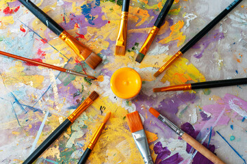 Brushes and a jar of yellow paint on the canvas of an artist covered with paints