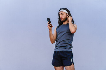 latino hispanic long-haired male athlete listening to music or podcast on cell phone with wireless...