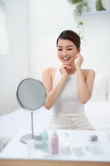 Image of pleased asian woman smiling and looking at mirror