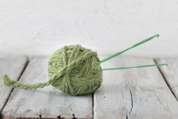 green yarn ball and crochet hook on white wood table 