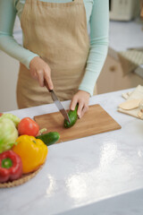 Beautiful young woman is preparing vegetable salad in the kitchen