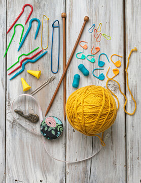 yellow yarn ball and wood knitting needles, embroidery scissors, locking stitch markers, yarn needles  on white wood table, ready for knit  