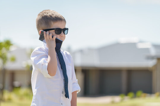 Boy standing and talking on the mobile phone while wearing business attire with sunglasses on a bright summer day