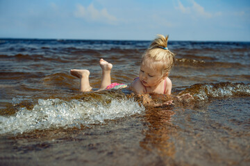 Little girl lying in sea looking at waves. Sunny day on the beach