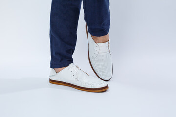 Men's feet in white everyday sneakers made of natural leather on lacing.