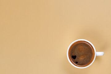 A cup of freshly brewed coffee with hearts inside on a beige background.