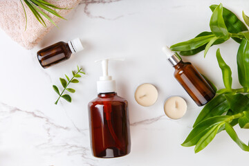 Top view Spa and bath cosmetics on white marble background: serum and face gel, towel rolls, soap. Natural face care products in bathroom. Eco-friendly cosmetics with plants. Natural beauty