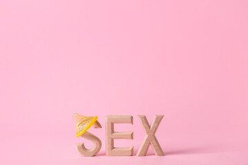Word SEX with condom on color background