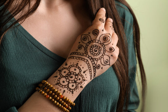 Woman with beautiful henna tattoo on hand against green background, closeup. Traditional mehndi
