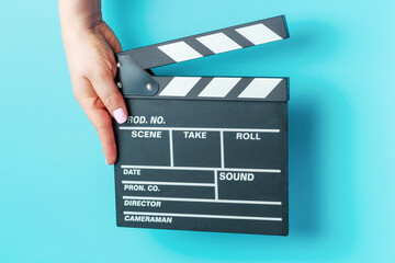 Female hand holding movie clapper board close-up on blue background.
