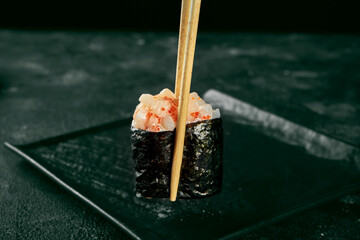 Gunkan maki sushi with salmon and spicy sauce on a black board with ginger and wasabi. Japanese kitchen. Food delivery. Black background. Sticks hold sushi © ismishko