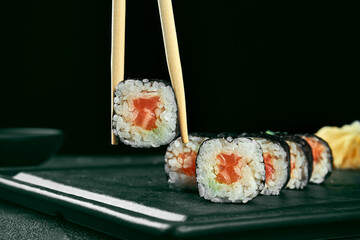 Maki sushi roll with salmon. Classic Japanese cuisine. Food delivery. Black background. Sticks hold sushi