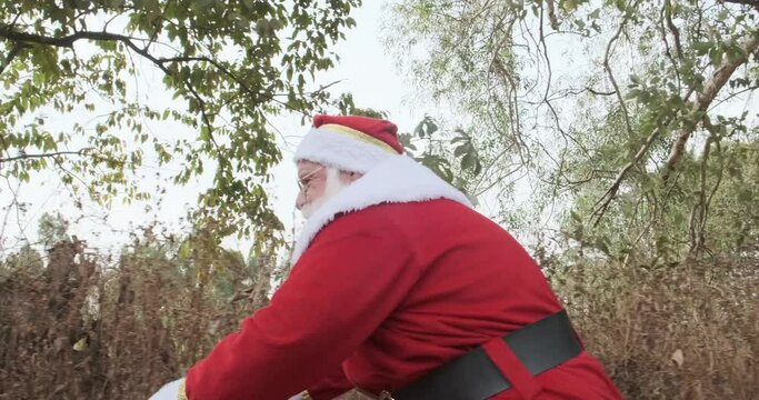 Santa Claus riding a bicycle on dirt road. 4K.