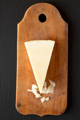 Pecorino Romano Cheese on a rustic wooden board on a black surface, top view. Flat lay, overhead, from above.