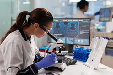 Healthcare scientist researcher vaccine looking at sample through microscope to check for mutations. Medicine, biotechnology researcher in advanced pharma lab, examining virus evolution.
