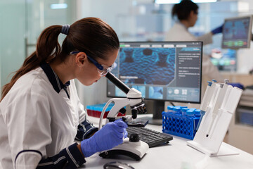 Healthcare scientist researcher vaccine looking at sample through microscope to check for...