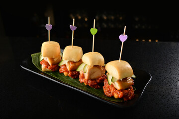 grilled chicken breast with spicy red sauce mini burger bun appetiser canapés in dark bar counter...