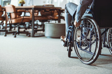 Cropped shot of disabled businessman in wheelchair. Businessman in wheelchair, hand on wheel close up, office interior on background.  A man on a wheelchair Recovery