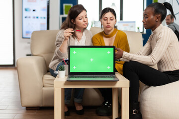 Laptop with green screen on table in start up company with multiethnic diverse coworkers working...
