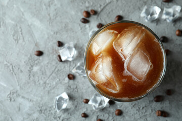 Glass of ice coffee, beans and ice on grey textured table