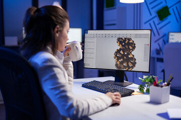 Focused architect working at new project using computer doing gear prototype late at night sitting at desk in start-up office. Industrial woman engineer studying on pc for development cad software