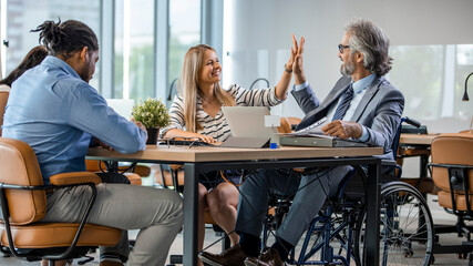 Disabled Male Manager Sitting With His Colleagues At Workplace. Disabled businessman working in an...