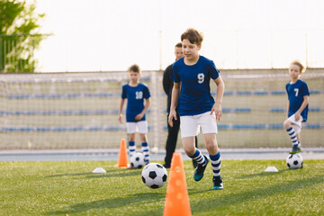 Obraz premium Happy boys practicing football with coach on a sunny day. Group of children playing soccer on training session. Kids in football club wearing blue jersey shirts and soccer kits.
