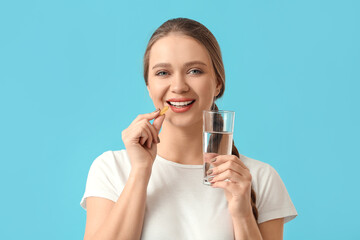 Young woman taking fish oil on color background - obrazy, fototapety, plakaty