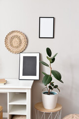 Table with houseplant and frames near light wall
