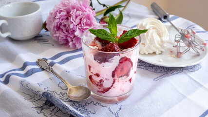 Pink, Eton mess dessert with strawberry, cream and white egg meringue. Whipper aside on a table with blue and white cloth.  Close up. Food styling