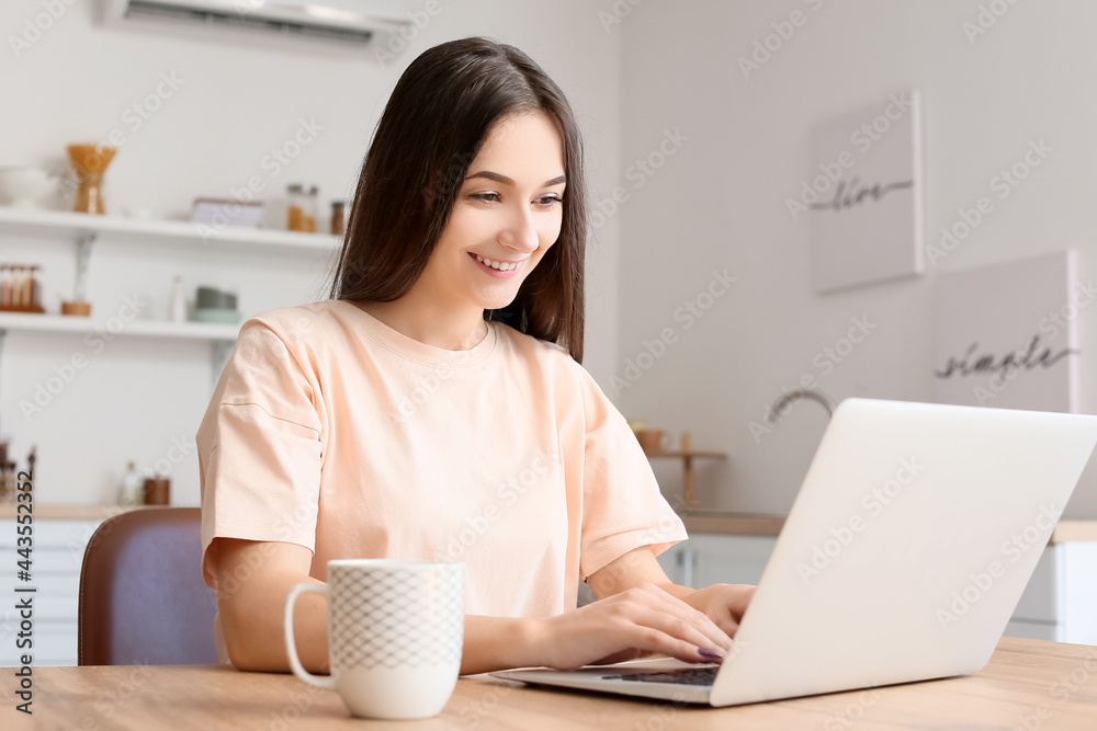 Canvas Prints Young woman using laptop in kitchen