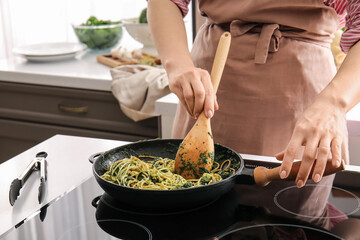 Woman cooking tasty pasta with spinach in kitchen