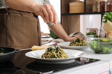Woman cooking tasty pasta with spinach and cheese in kitchen
