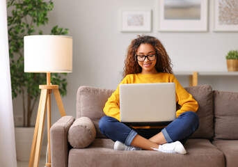 Smiling african american young woman using laptop while working remotely or studying online from...