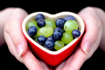 Fresh grapes and blueberries in heart shaped dish held by young girl