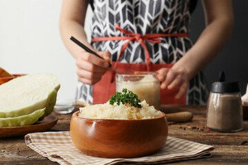 Woman preparing tasty sauerkraut at kitchen table, closeup