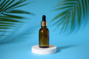 Amber glass dropper bottle with metallic lid on on the white podium with tropical leaves on background. Skincare products , natural cosmetic. Beauty concept for face and body care