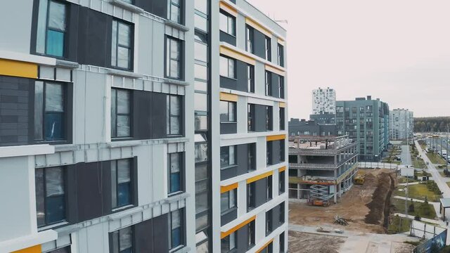 Construction site, building work process modern an apartment panel house. Unfinished structure city block of flats, white facade with mansard roofs and windows on background sunset, top view