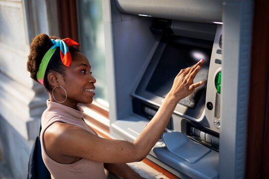 Beautiful african women using ATM machine. Attractive young woman withdrawing money from credit card at ATM.
