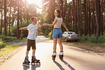 Outdoor shot of mother and son on roller skates having together, woman with her child dancing while...
