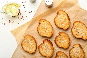 Wooden board with tasty toasted bread on light background