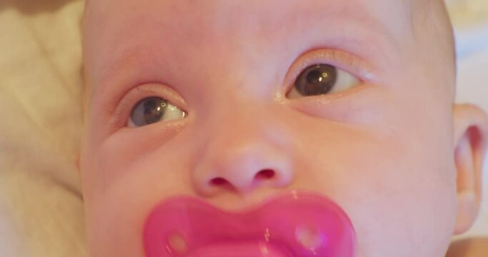 the face of a small funny and cute baby with a pacifier who looks up in surprise. close-up portrait.