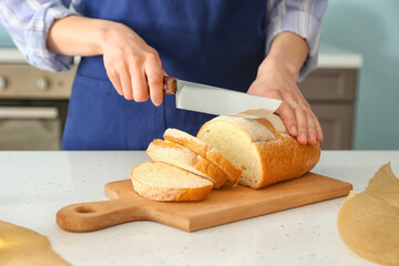 Female chef cutting fresh bread on kitchen table, closeup