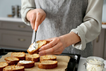 Female chef preparing toasts with cheese on kitchen table, closeup