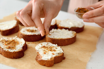 Female chef adding spices to toasts on kitchen table, closeup
