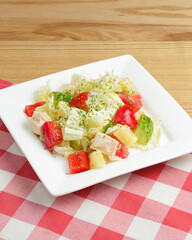 Healthy vegetarian salad on white plate over wooden table with red plaid tablecloth.