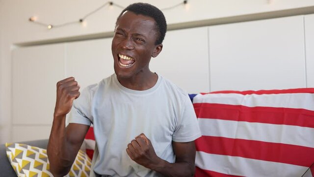 Portrait of a young African-American guy sitting on the sofa at home exults for success after reading the good news.