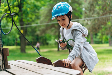 Brave, little boy climbs a suspension road in a rope park. The child actively spends time.