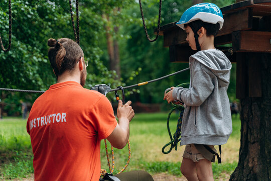 Instructor helps the boy and shows him how to use the rope properly. The child actively spends time outdoors