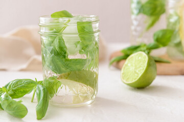 Glass of lemonade with basil on light background